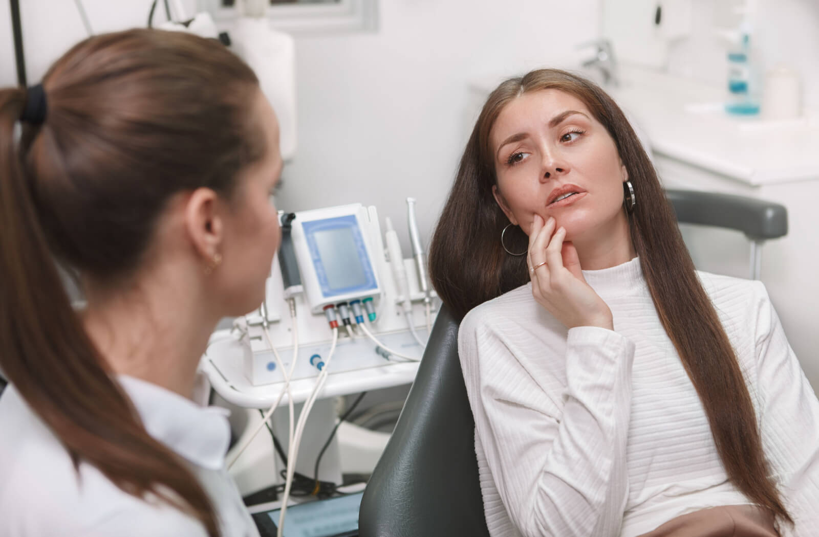 A patient in a dental chair rubbing their jaw while talking to their dentist about possible treatments like Botox.