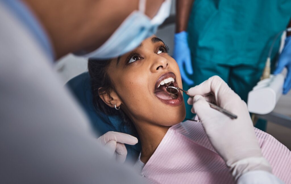 A dental hygienist uses a small mirror to examine their patient's mouth after their guided biofilm therapy cleaning.
