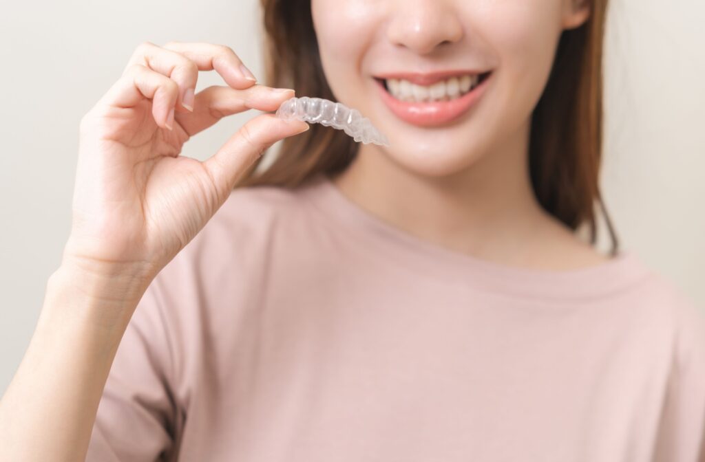 Smiling patient holding a clear Invisalign tray.