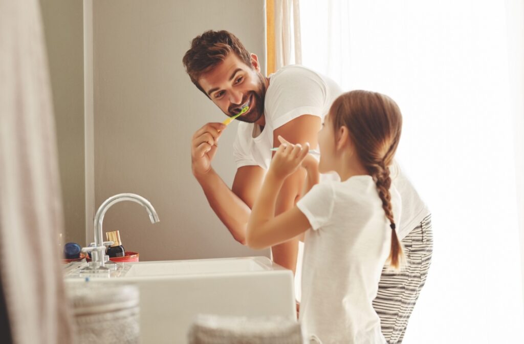 Father and young daughter brushing teeth together in the bathroom.