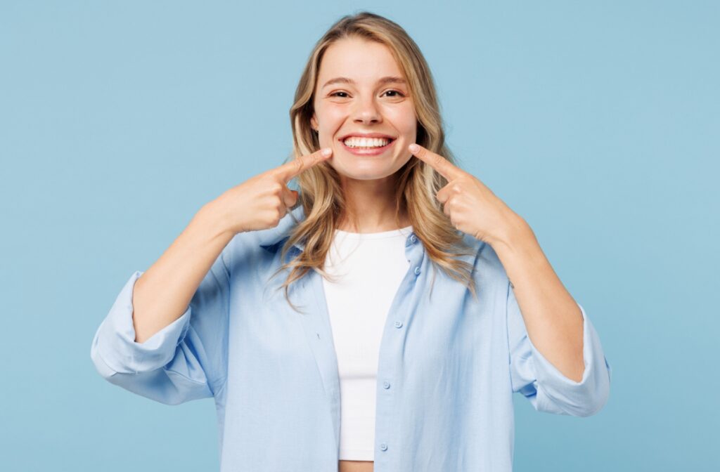 An adult smiles brightly while pointing to their straight teeth.