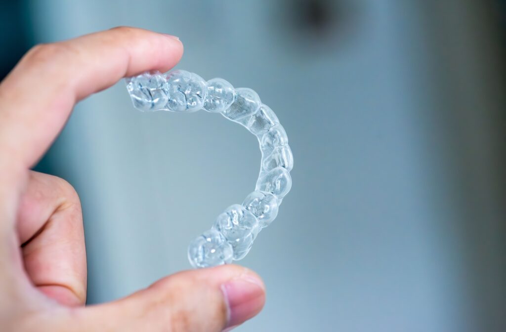 An Invisalign clear aligner being held between a pointer finger and thumb.