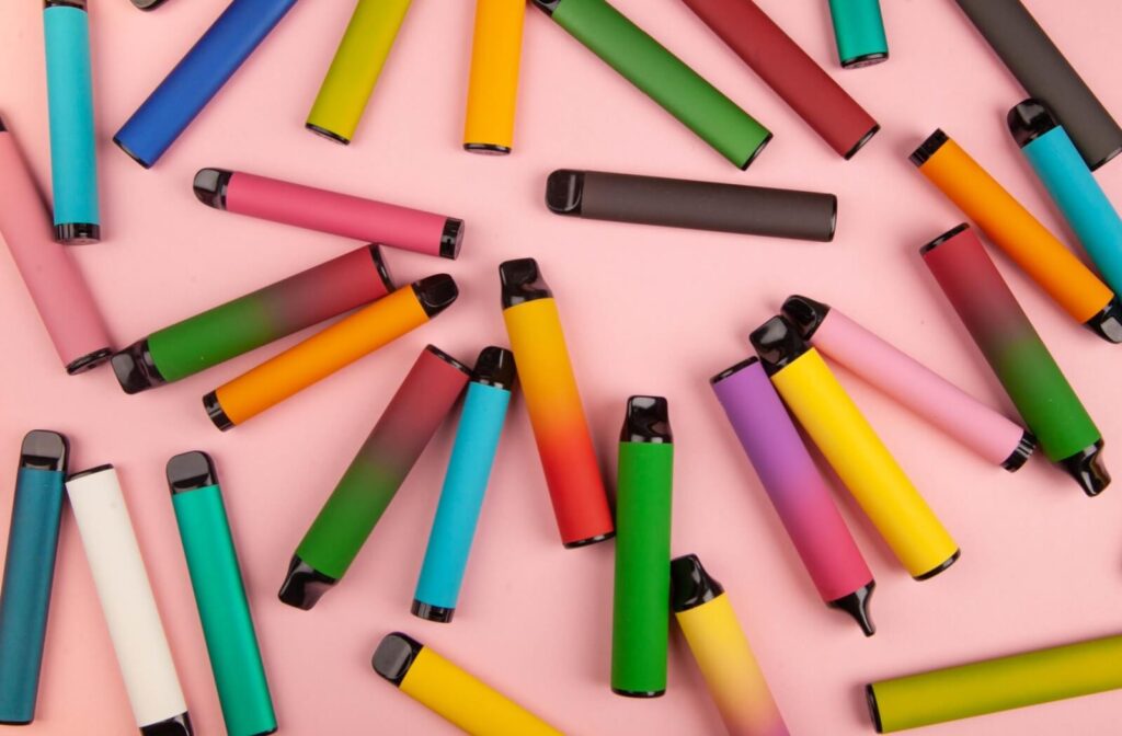 Various colourful vaping devices on a pink surface.