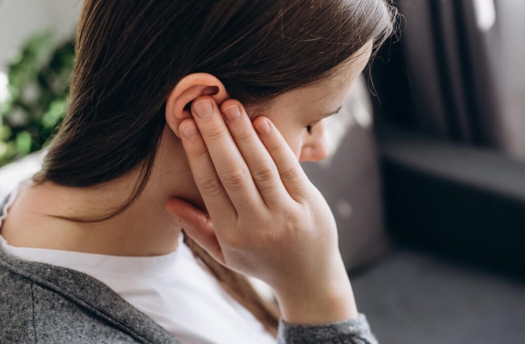 A close-up of a woman touching her ear and jaw area, indicating pain or discomfort in the TMJ.